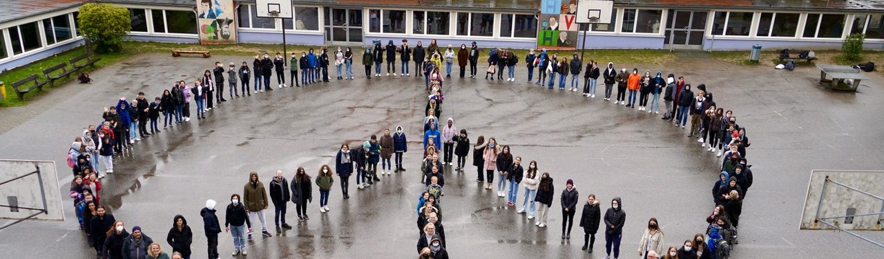Die Schülerinnen und Schüler bilden im Mai 2022 ein Peace-Zeichen auf dem Schulhof