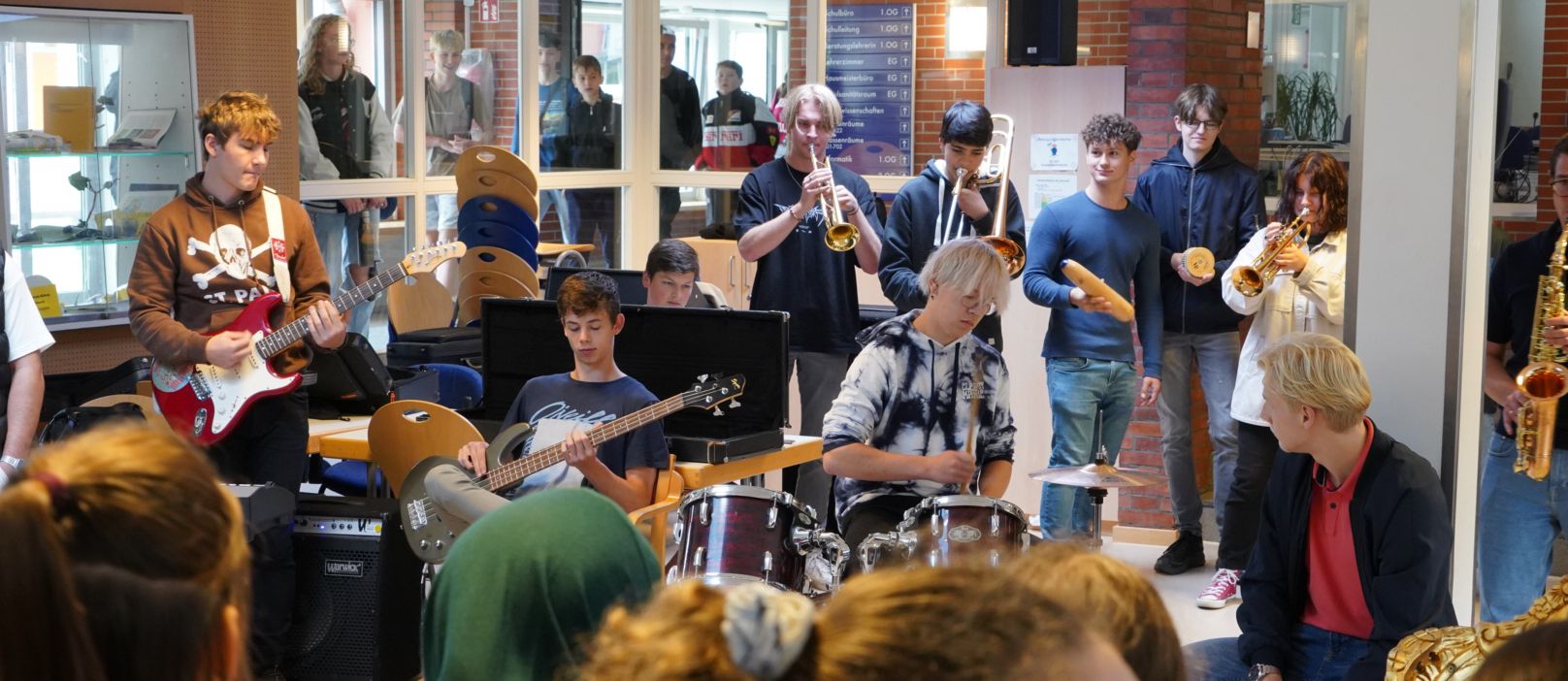 Eine Schülerband mit Trompeten, E-Gitarre, E-Bass und Schlagzeug spielt in der Pausenhalle