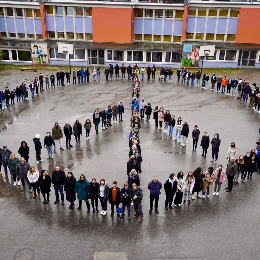 Die Schülerinnen und Schüler bilden im Mai 2022 ein Peace-Zeichen auf dem Schulhof